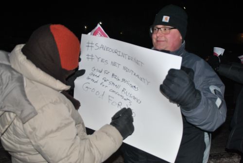 Tim Hoye holds up a sign for a fellow protester - photo by C.S. Hagen