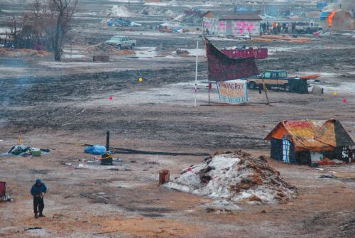 A lone activist starts the day with singing as a building burns (upper right) on the day of eviction from Oceti Sakowin - photograph by C.S. Hagen