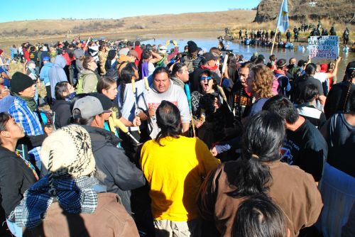 Drums beat while activists face police in ice cold water during the Dakota Access Pipeline controversy - phtograph by C.S. Hagen