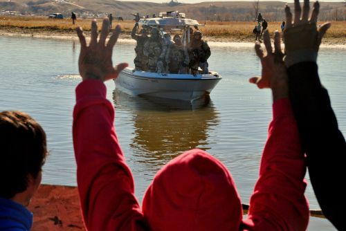 Activists at Standing Rock with raised hands before police and others along far shore - photograph by C.S. Hagen