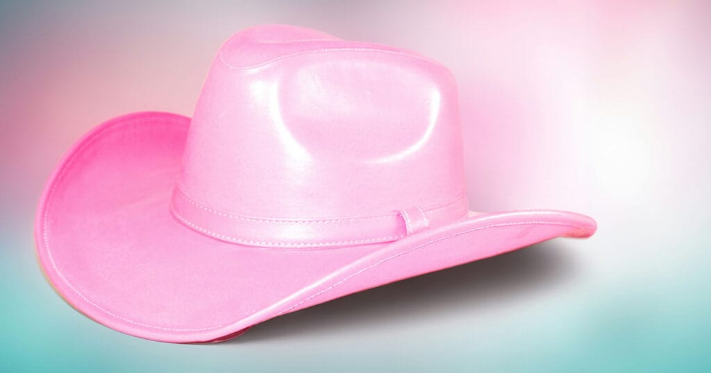 A pink leather cowboy hat resting on a soft pastel pink and blue background.