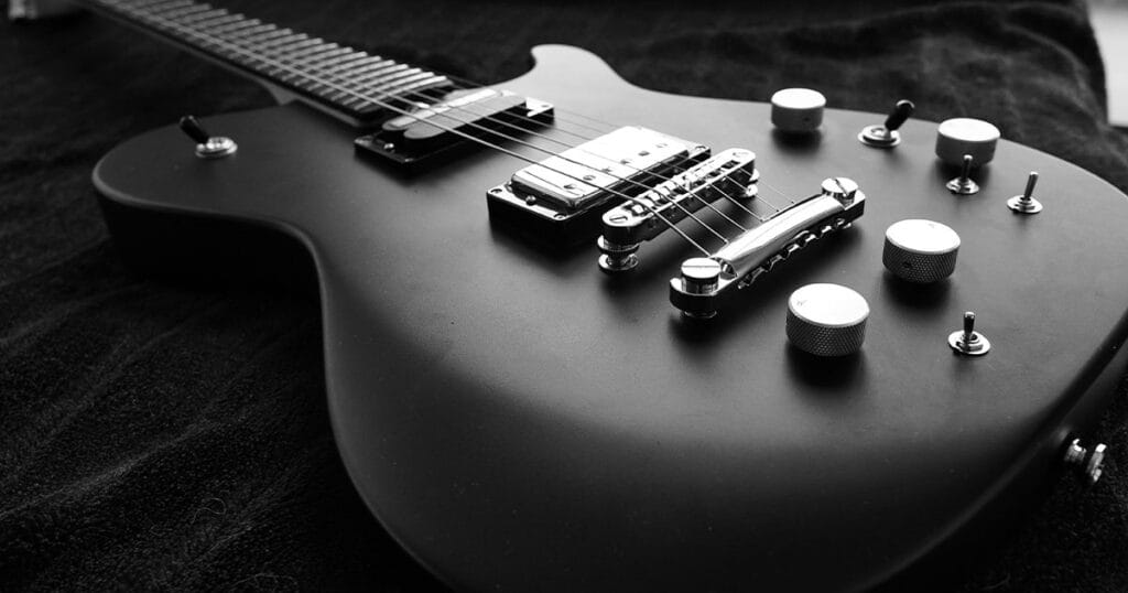 A black electric guitar photographed close up in black and white, showing the pickups, bridge and control knobs.