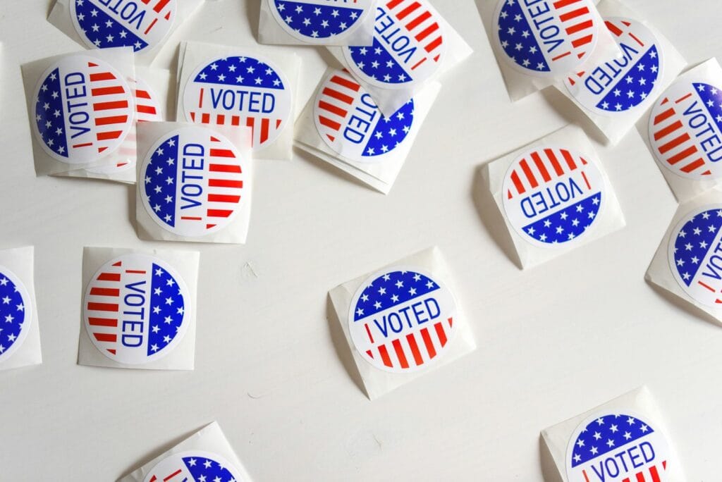 Red, white and blue “I Voted” stickers scattered across a white surface.