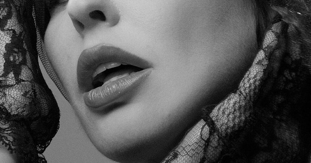 Black-and-white close-up of a performer's lips and jaw, framed on both sides by black lace.