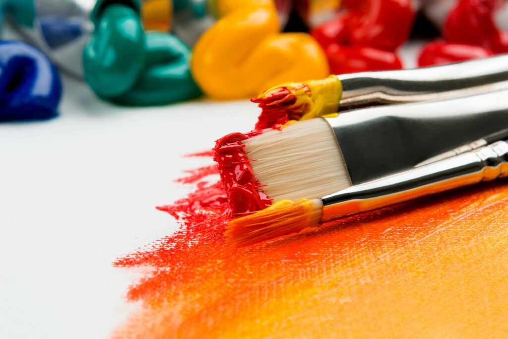 Paint brushes applying red and orange paint on canvas